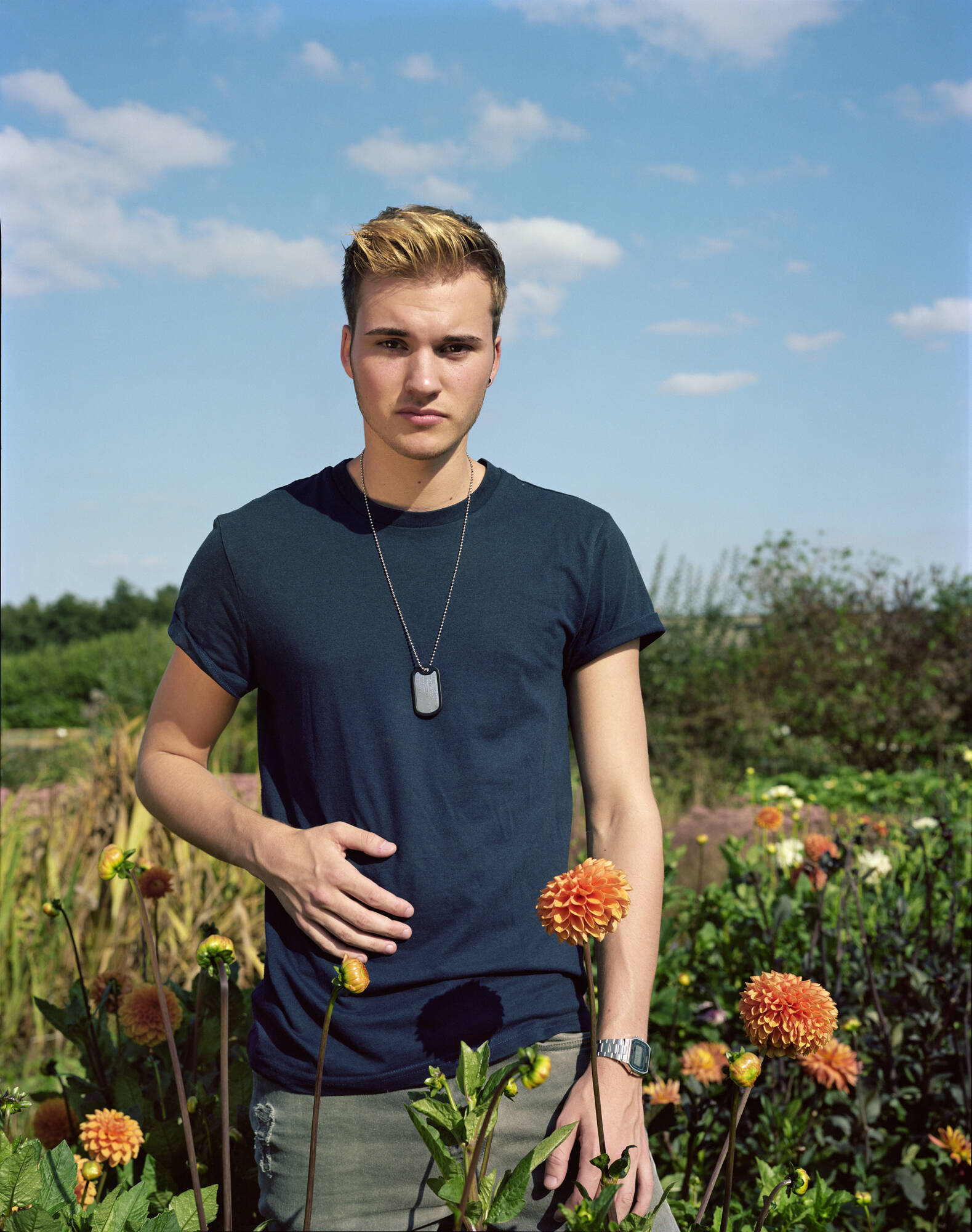 Color photograph of a person in a blue shirt standing in a field of flowers, blue sky behind them.